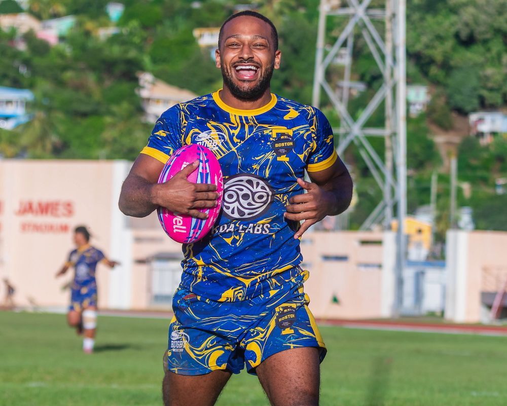Smiling athlete in blue and yellow kit holding a pink rugby ball on a field
