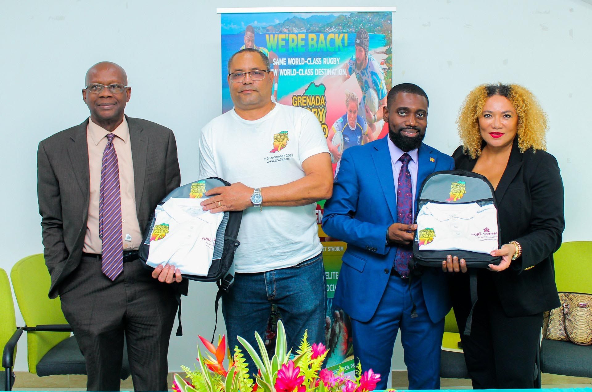 Four people posing with framed certificates in front of a banner, with flowers in the foreground.
