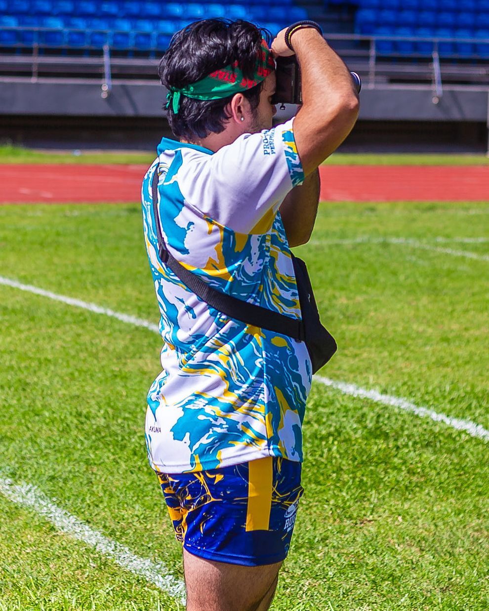 Athlete in colorful uniform and green headband raising arms on a sunny sports field