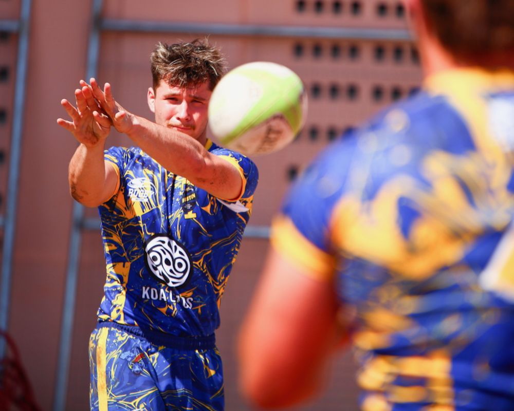 Athlete in blue-yellow uniform reaching for a flying ball during an outdoor game