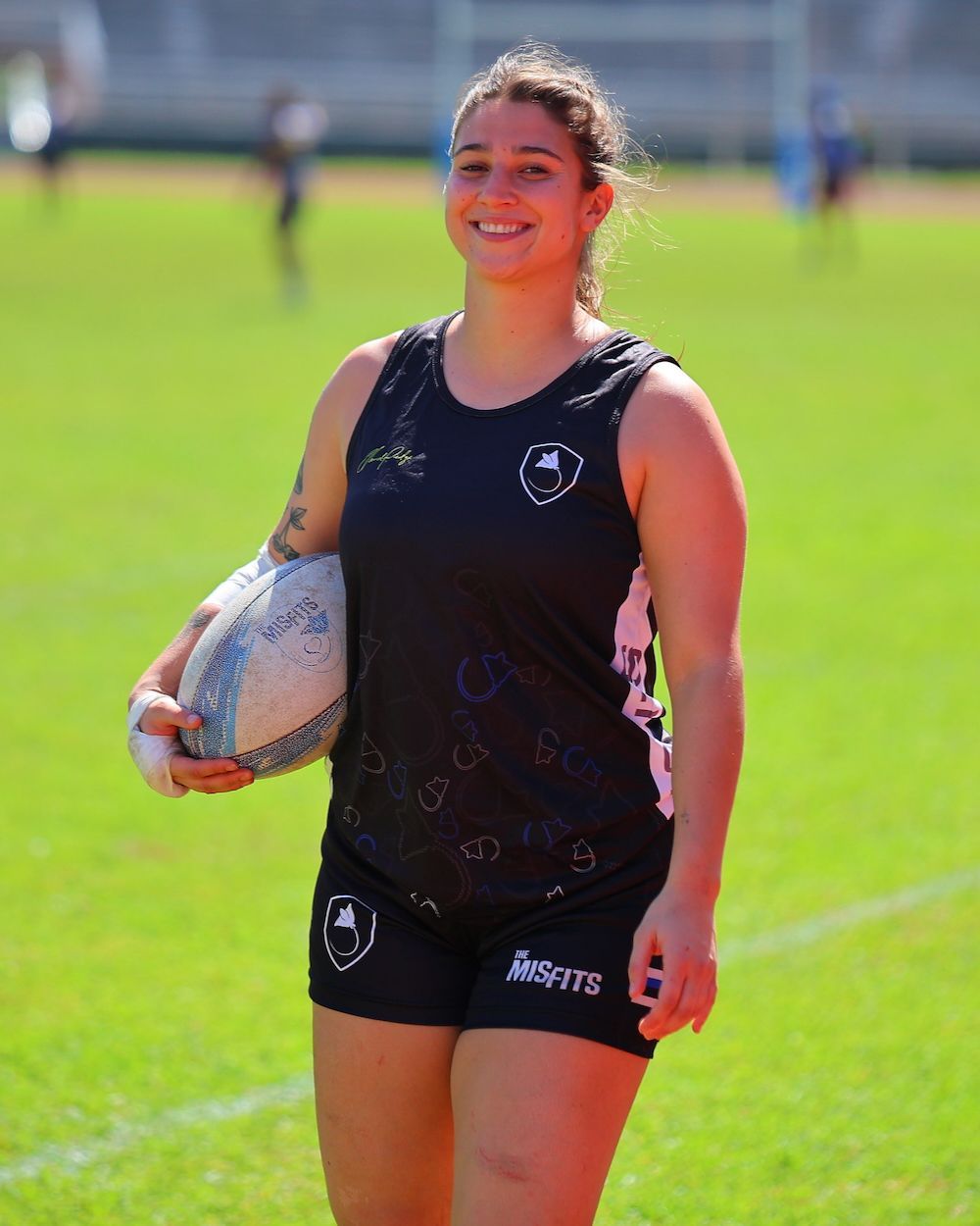 Smiling athlete in black sportswear holding a rugby ball on a grassy field