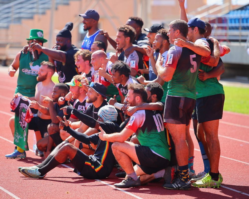 Group of athletes in green jerseys posing together on a running track, smiling and celebrating.