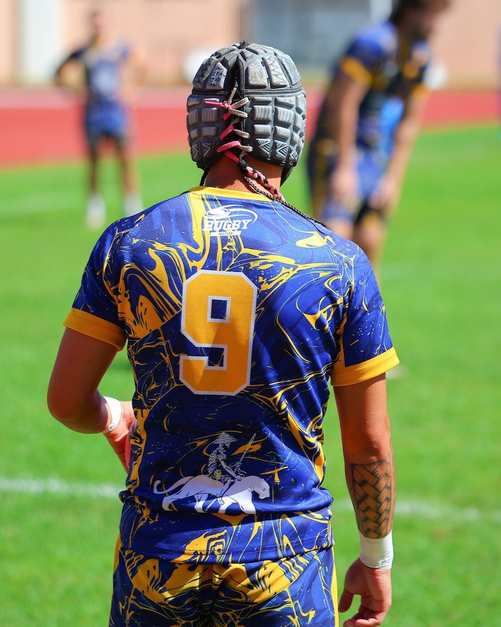 Rugby player in blue and gold jersey with number 9 stands on a field during a match