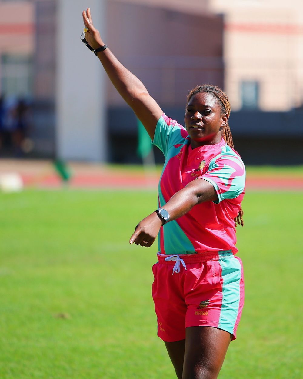 Person in pink and teal sportswear signaling on a field, one arm raised