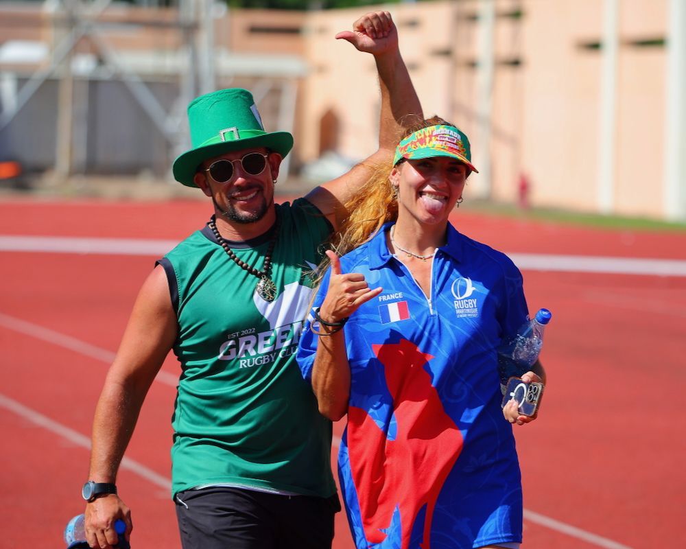 Two runners in colorful outfits smiling and posing on a red track, one with an arm raised.