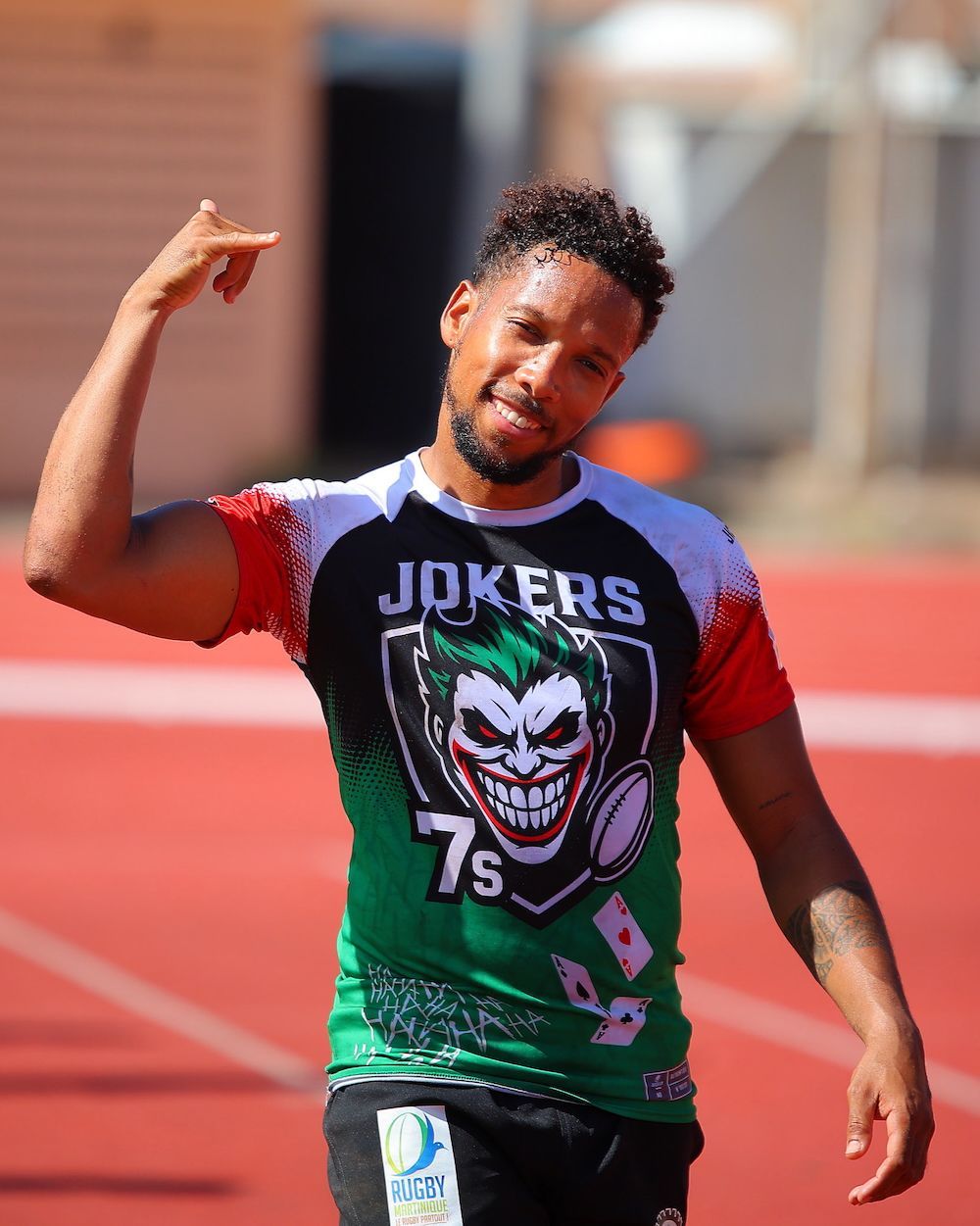 Runner in a green Joker jersey gesturing with one hand on a track.