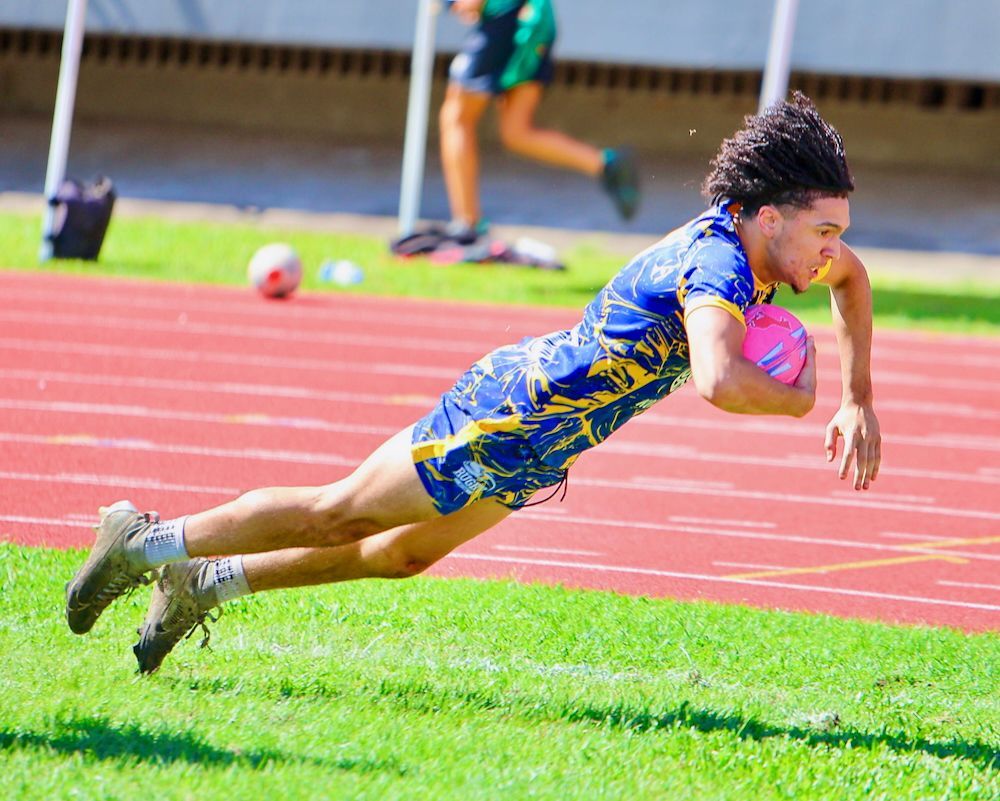 Athlete in blue and yellow uniform diving forward with a ball on a track field