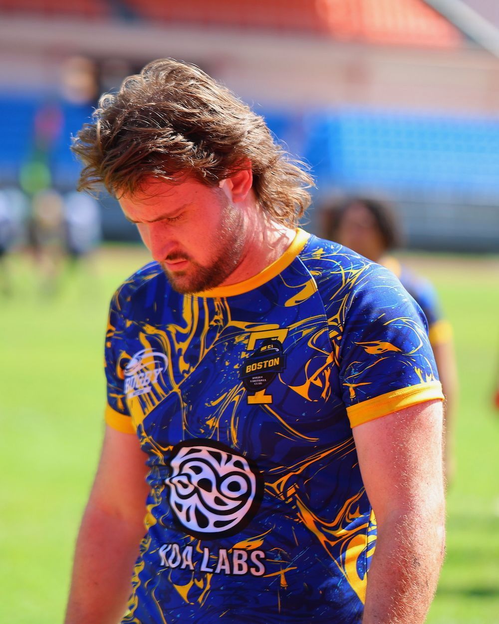Athlete in blue and gold jersey looking down on a sports field