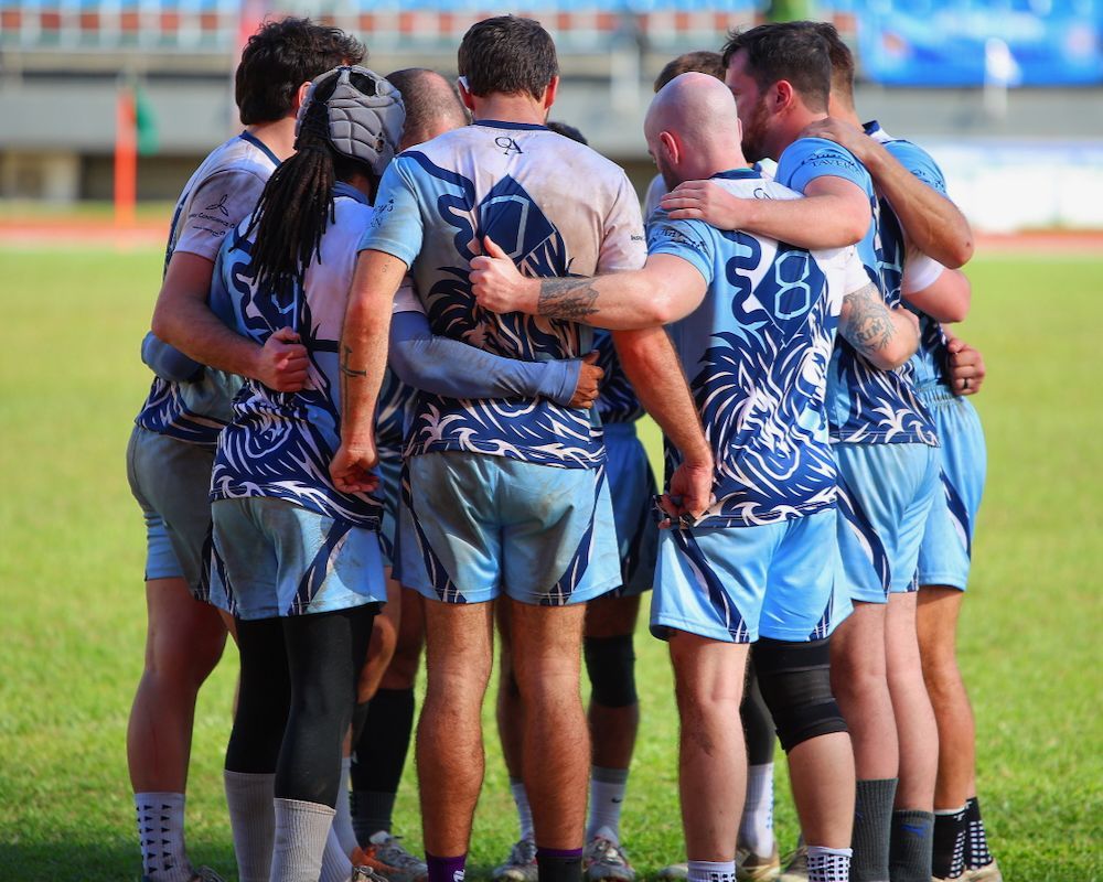 Rugby team huddled together on a grassy field in blue and white uniforms
