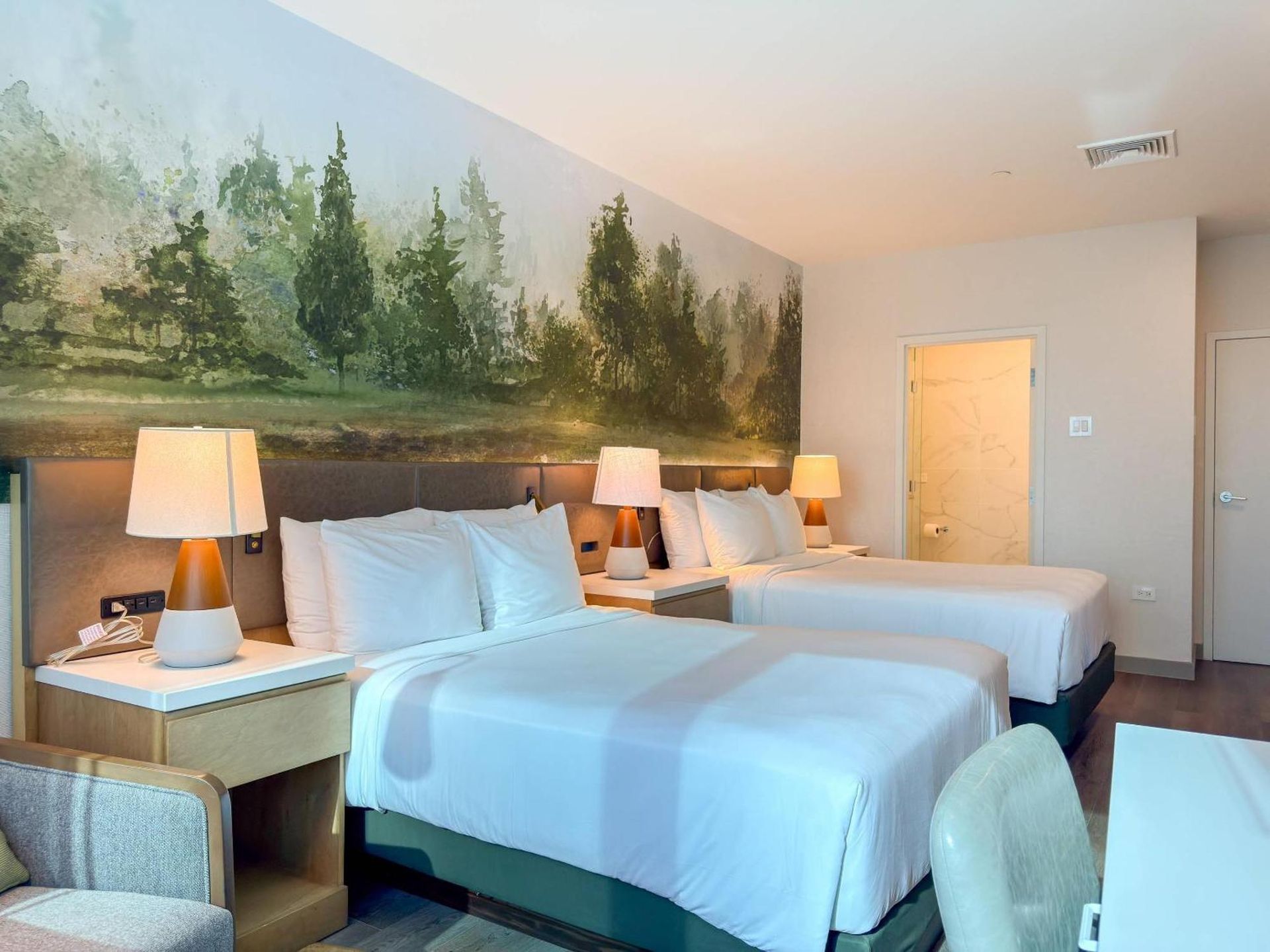 Wooden bed with blue bedding in a sunlit bedroom, with rugs, nightstand, and wall art