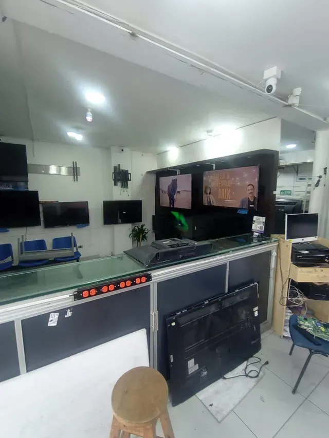 Sala de control de electrónica interior con monitores, consolas y sillas bajo luces brillantes del techo.