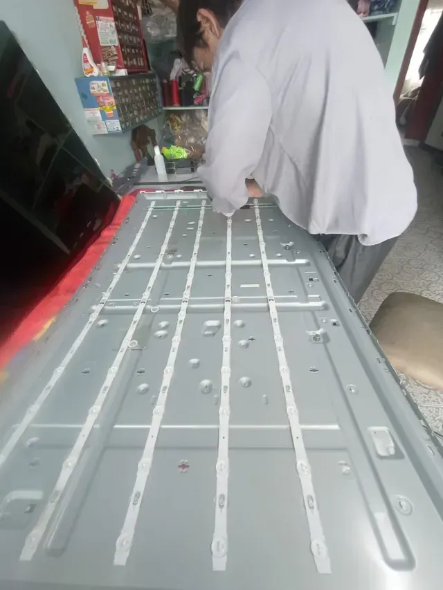 Persona inclinada sobre un panel gris de un vehículo con franjas blancas en un taller o garaje.