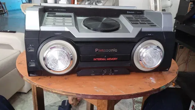 Radiocasete portátil negro con altavoces plateados y asa superior sobre una mesa de madera.