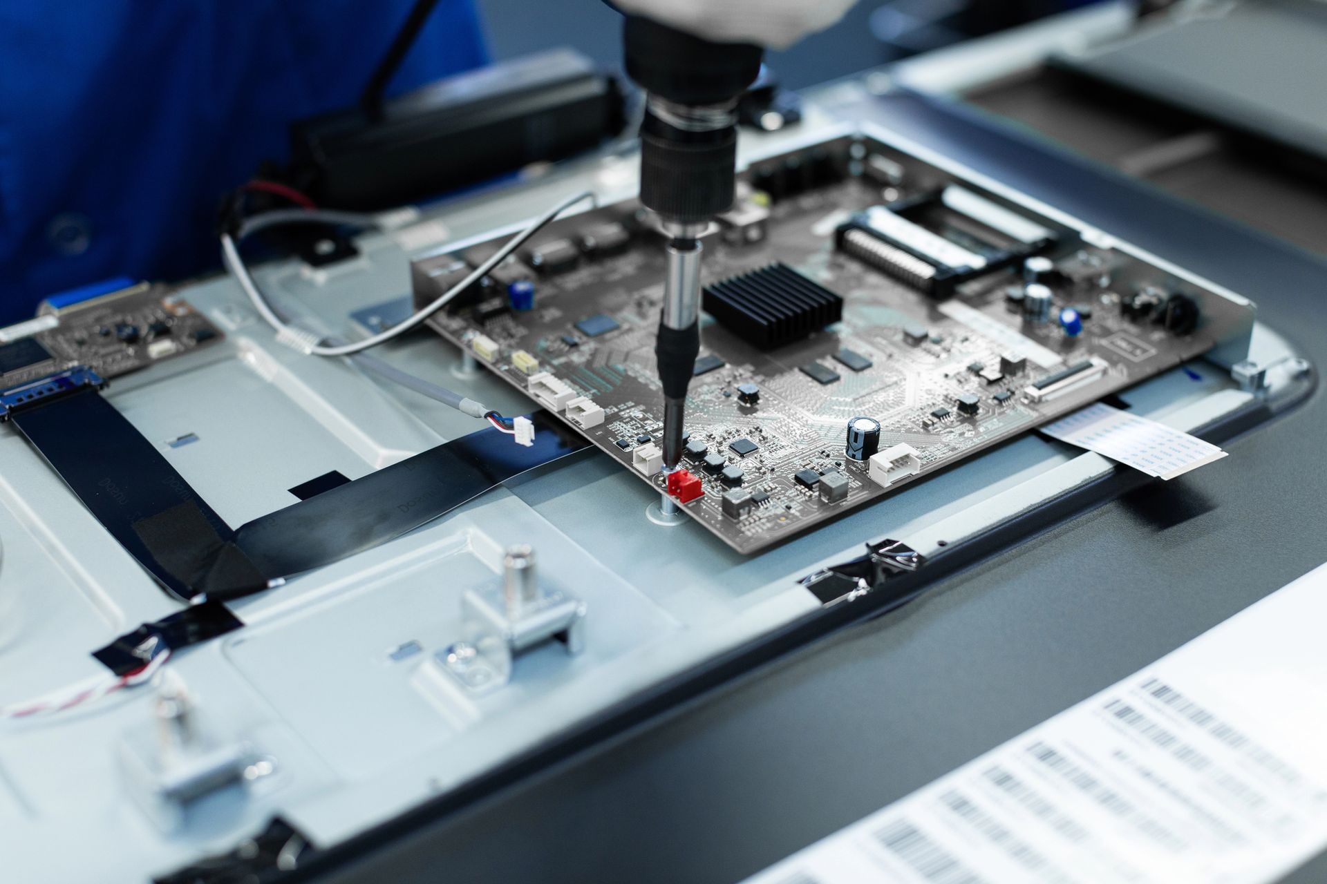Primer plano de un técnico reparando una placa de circuito impreso en un banco de montaje de dispositivos electrónicos.