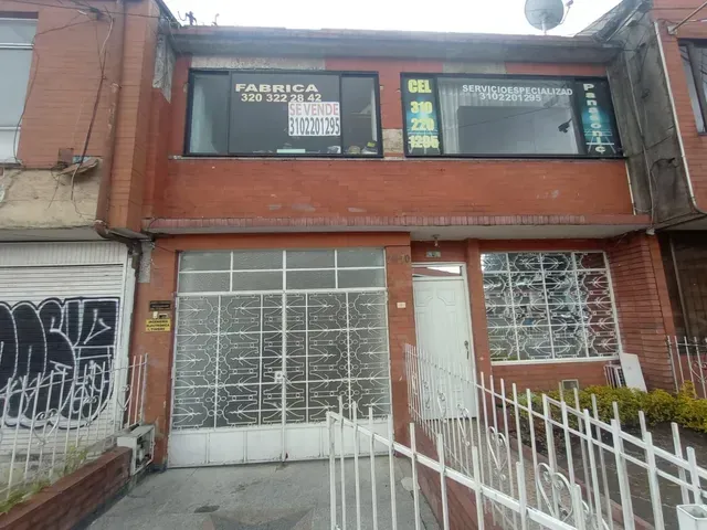 Local comercial de dos plantas de ladrillo rojo con puertas blancas estilo garaje y ventanas enrejadas, visto desde la calle.