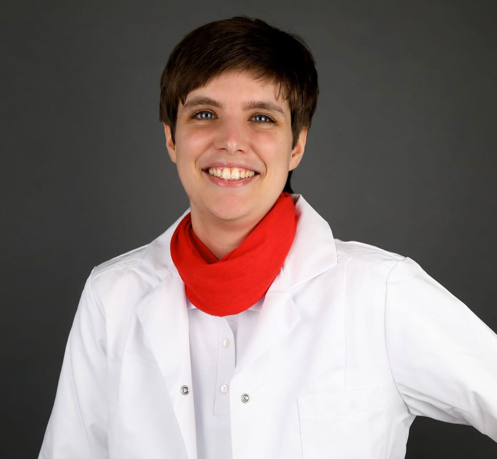 Eine Frau in einem weißen Laborkittel und einem roten Schal lächelt in die Kamera