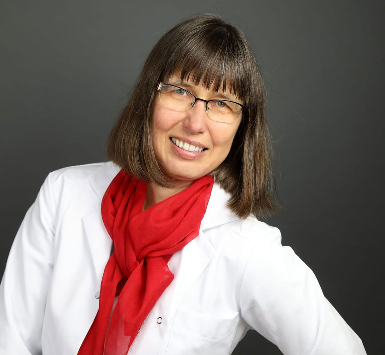 Eine Frau mit Brille und rotem Schal lächelt in die Kamera