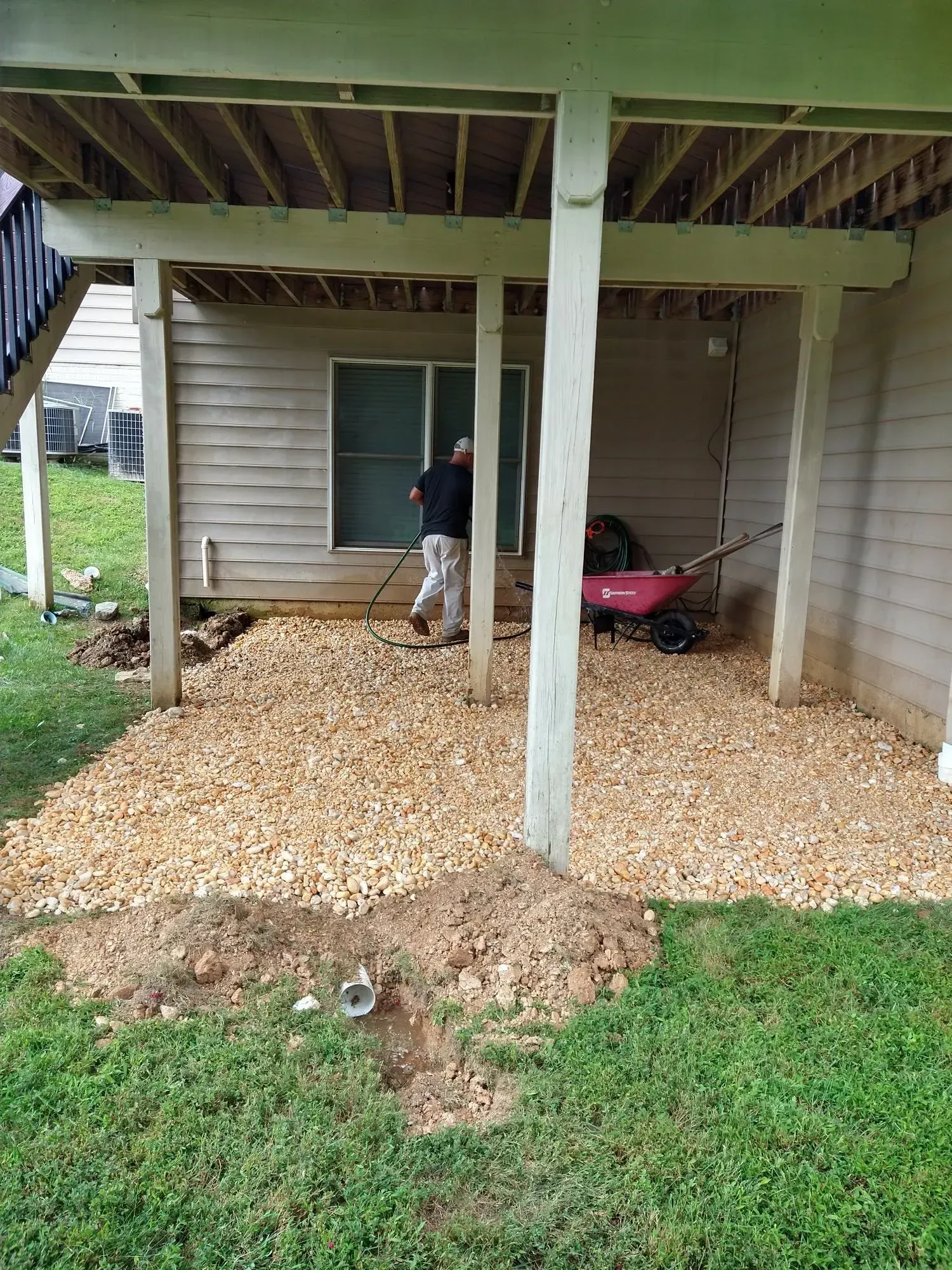 Person using a red wheelbarrow to spread gravel under a raised house porch.