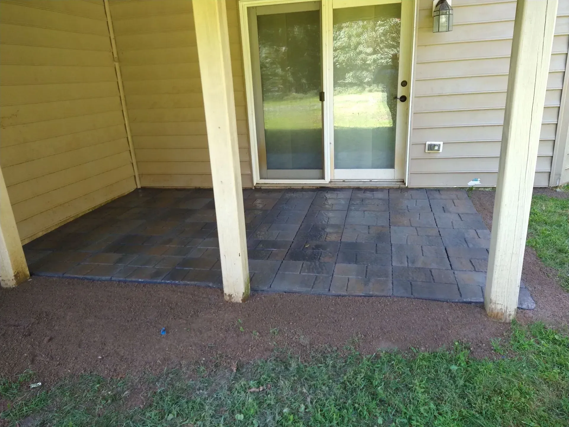 Covered patio with sliding glass door, tiled section, and gravel border beside a grassy yard