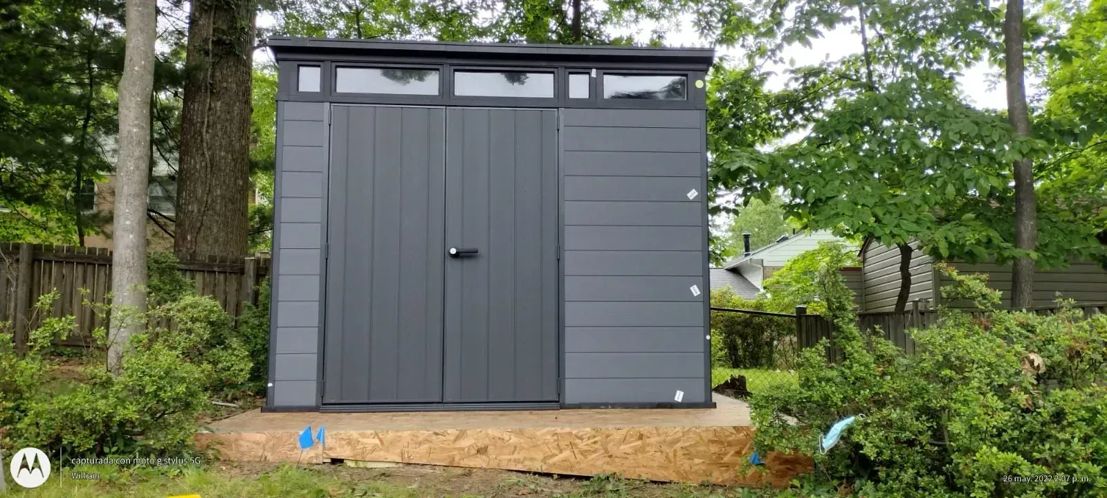 Gray shed with double doors on a gravel pad in a wooded yard