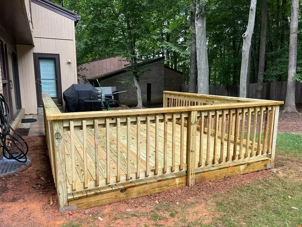 Wooden deck ramp with railings beside a house in a wooded backyard