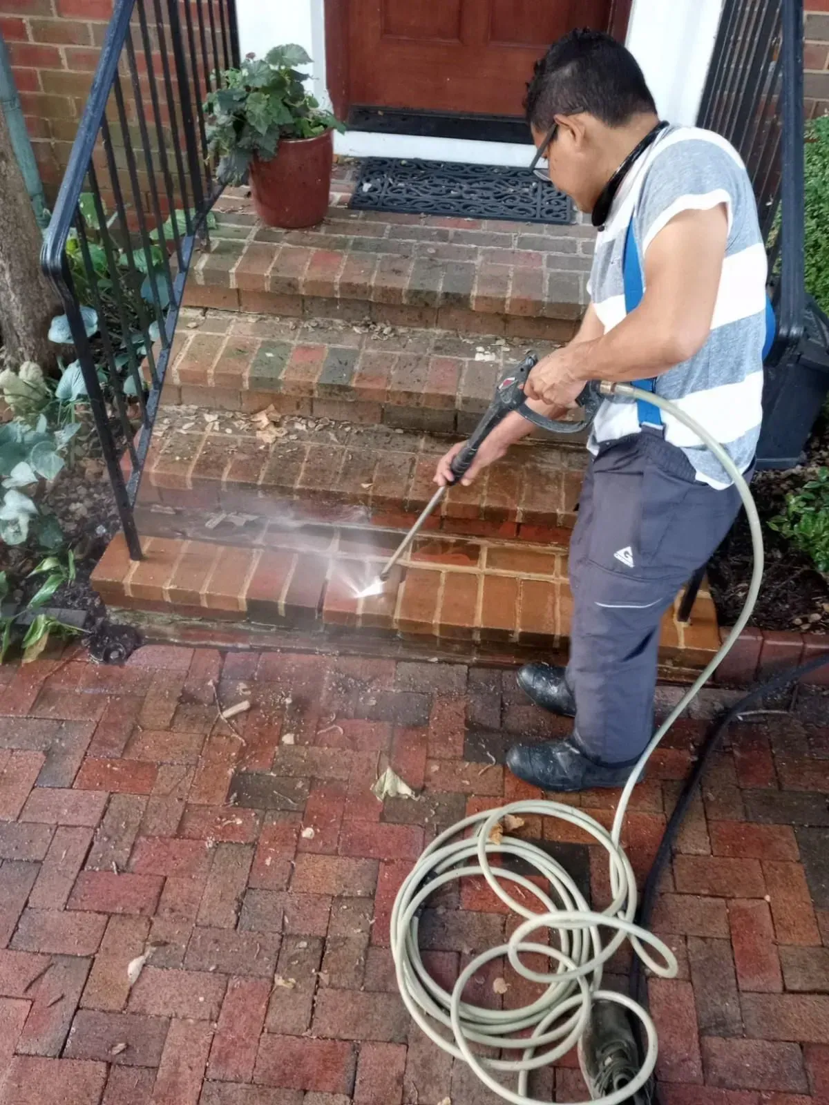Man pressure-washing brick front steps with a hose and spray wand.