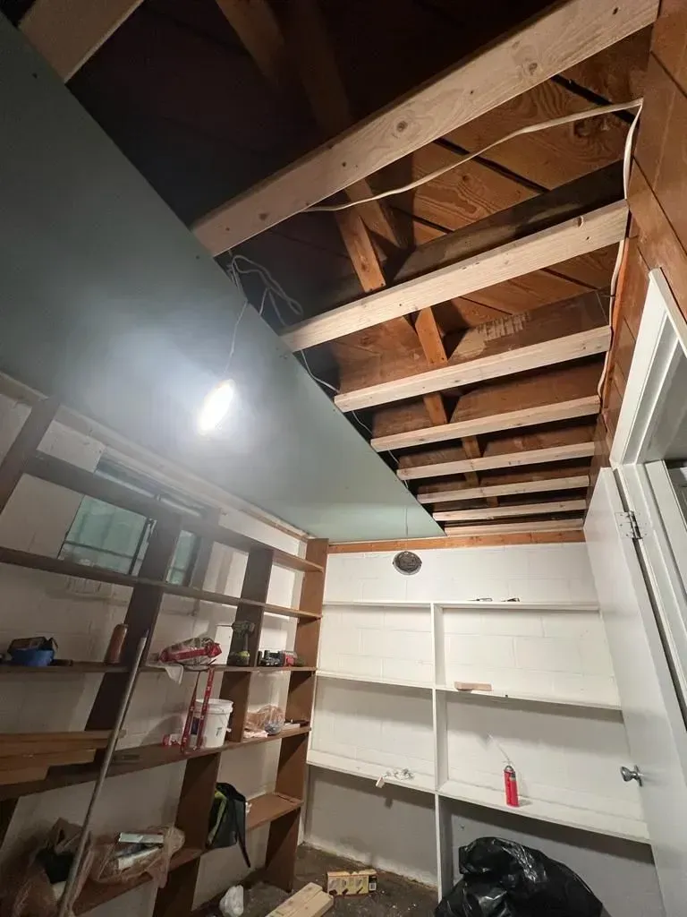 Small storage room with open ceiling beams, white shelving, and a wooden bookcase.