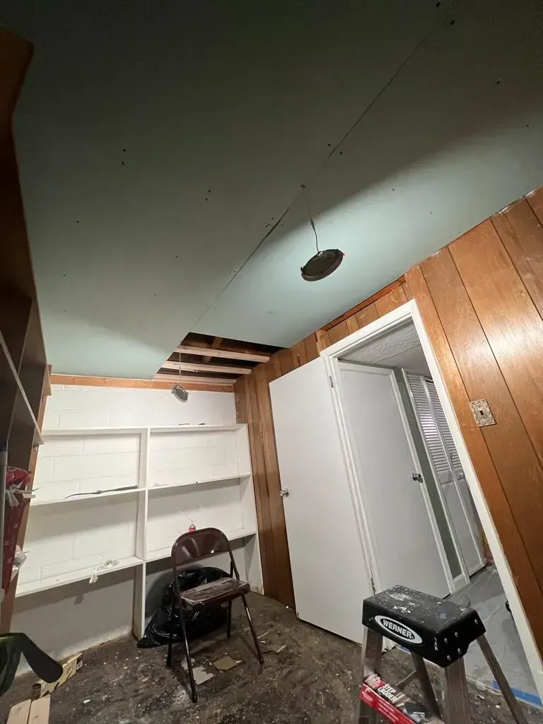 Small unfinished room with white shelves, exposed ceiling, and two chairs.