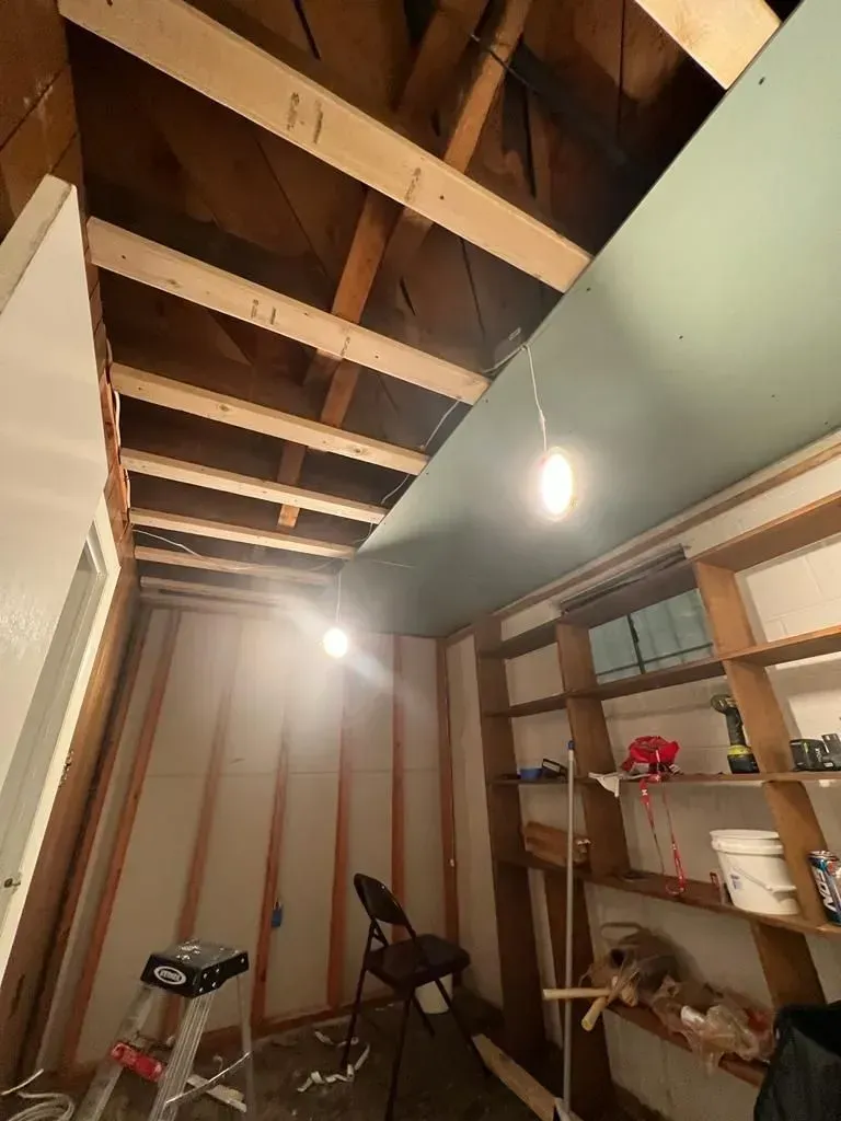 Narrow indoor hallway with exposed ceiling joists, hanging lights, and a shelving unit on the right.