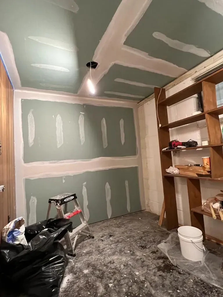 Partially finished room with green drywall, exposed shelves, tools, and construction debris on the floor.