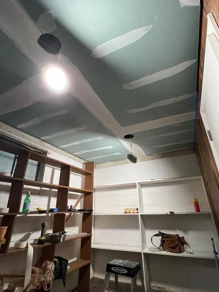Small room with shelves, ceiling lights, and a teal painted ceiling under repair