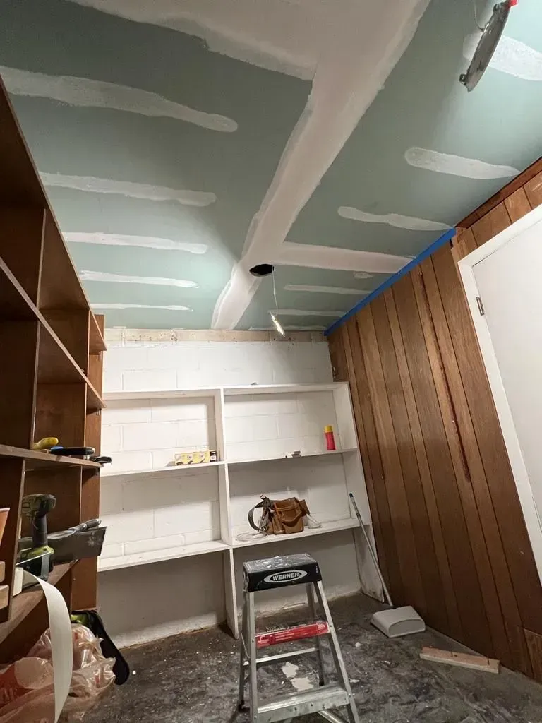 Partially finished room with drywall ceiling, shelves, ladder, and wood paneling on the right.