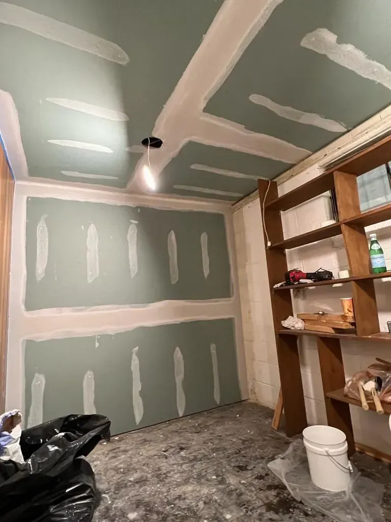 Partially finished room with green drywall, exposed shelves, and a white bucket on the floor.