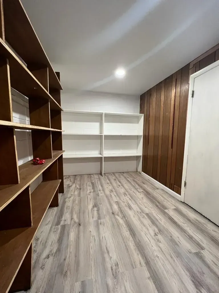 Empty walk-in closet with wood shelving, white built-in shelves, wood-paneled wall, and light gray flooring.