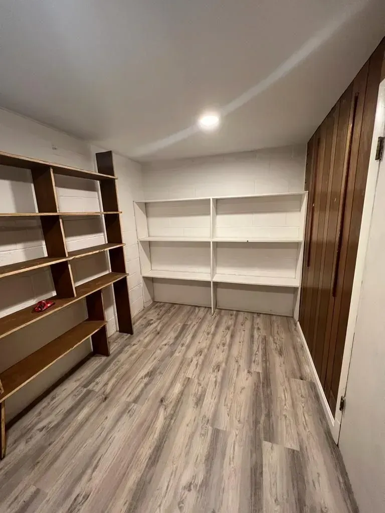 Empty closet with white shelves, wood flooring, and brown built-in cabinets under a ceiling light