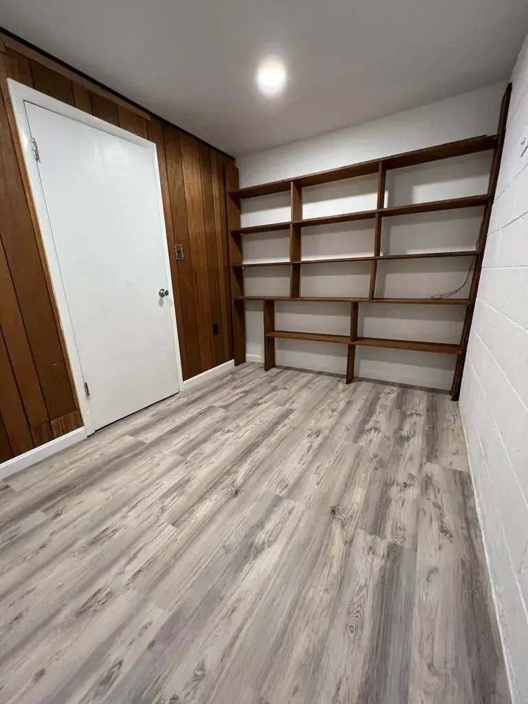 Empty room with white door, wood-paneled wall, and built-in shelves on the right.