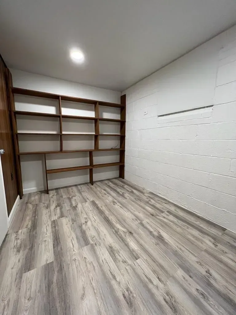 Empty room with light wood flooring, white walls, and built-in wooden shelves in the corner.