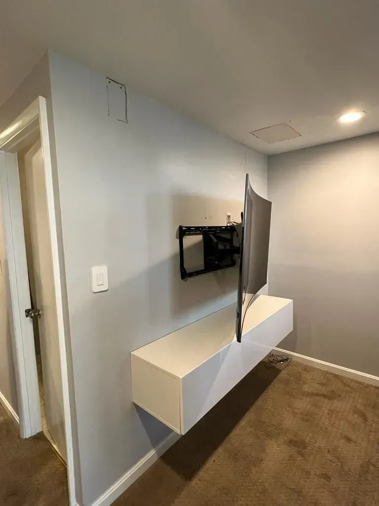 Hallway with wall-mounted TV and floating white cabinets on a gray wall, seen from a corner view