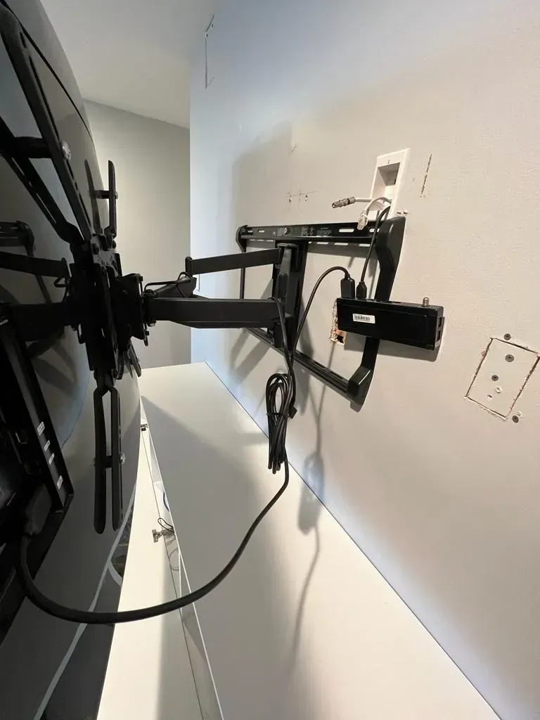 Wall-mounted TV bracket on a white wall, viewed from the side with cables visible