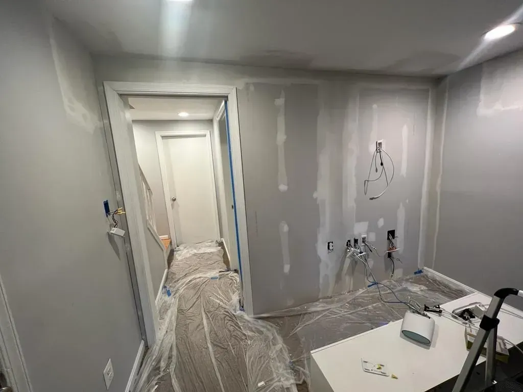 Partially renovated hallway with plastic-covered furniture, gray walls, and exposed wiring near a doorway