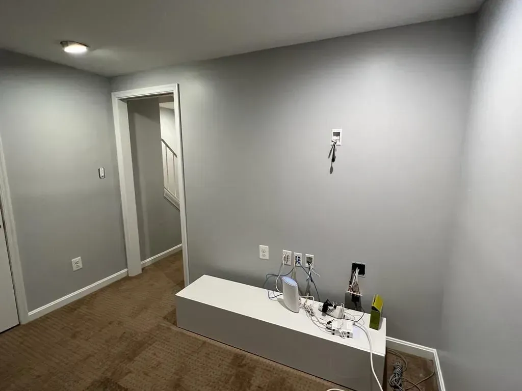 Empty gray room with wood floor, open doorway, and a white bench holding assorted items against the wall