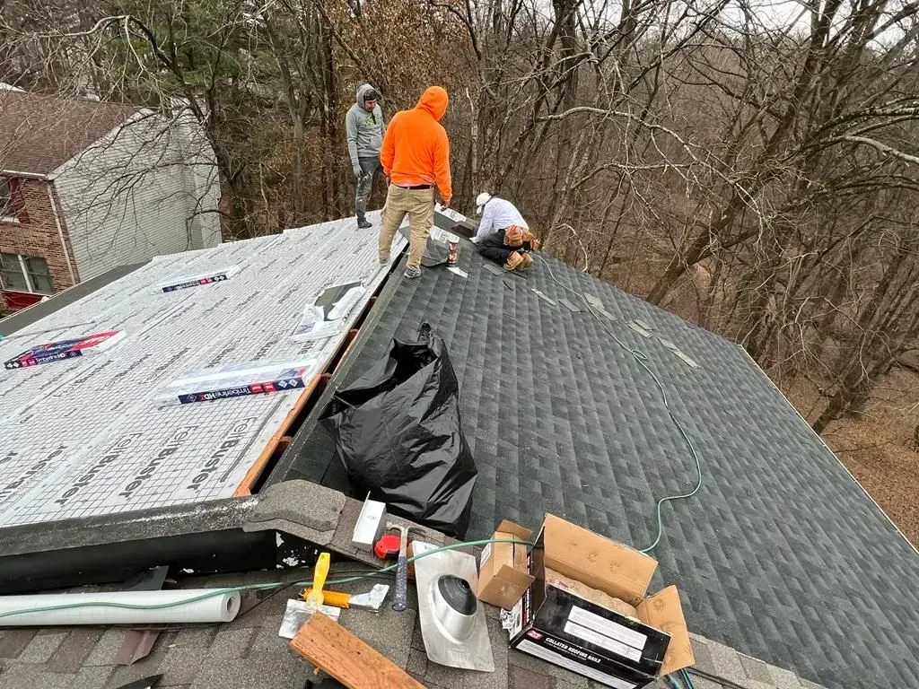 Two workers repairing a shingled roof, with one section covered in underlayment and tools nearby.