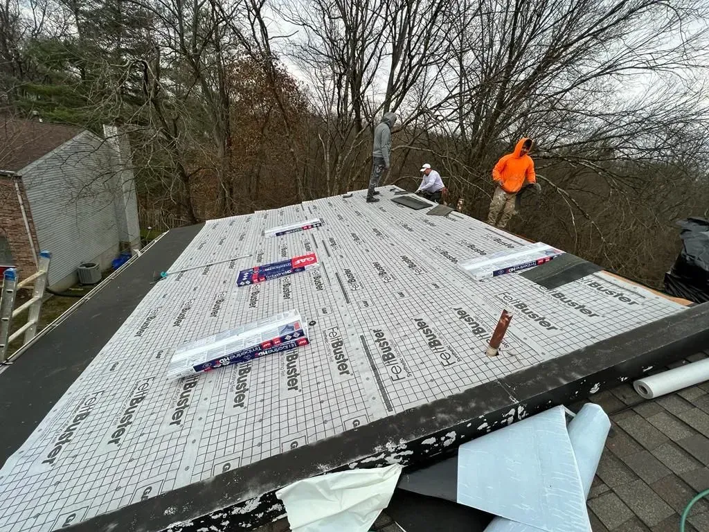Workers installing a white roof under construction, with one person in a bright orange jacket nearby