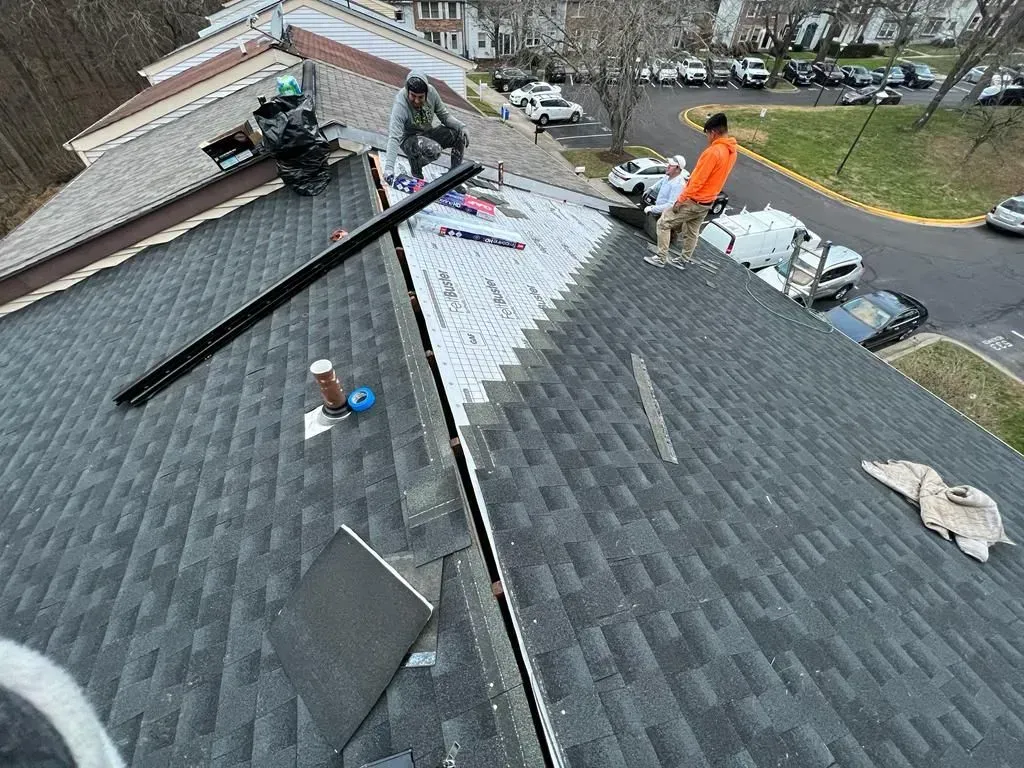 Roofers working on a gray shingled roof, with tools and materials scattered across the surface.