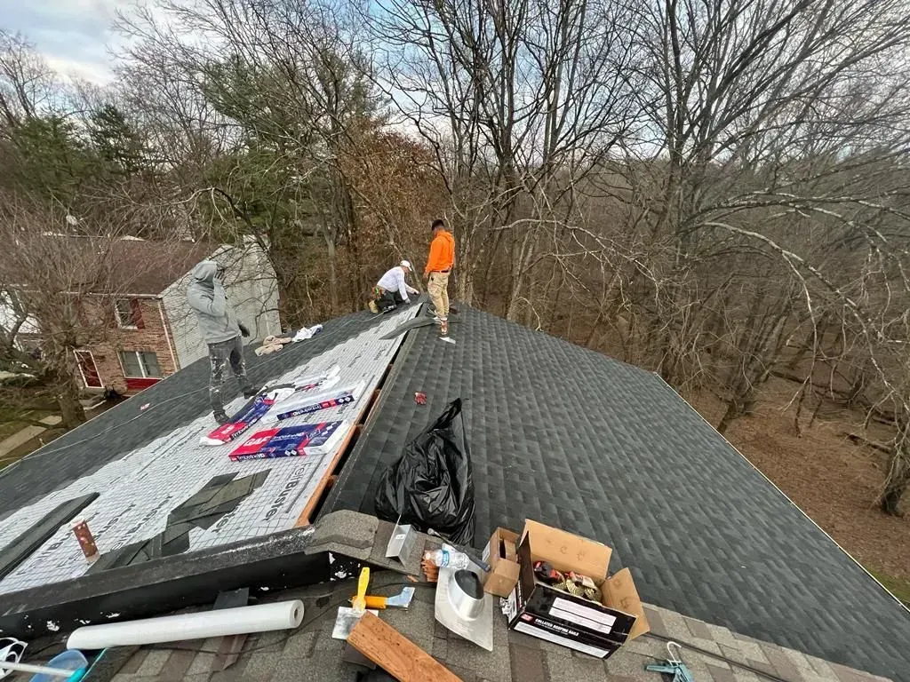 Workers repairing a steep shingled roof, with tools and materials spread across the top.