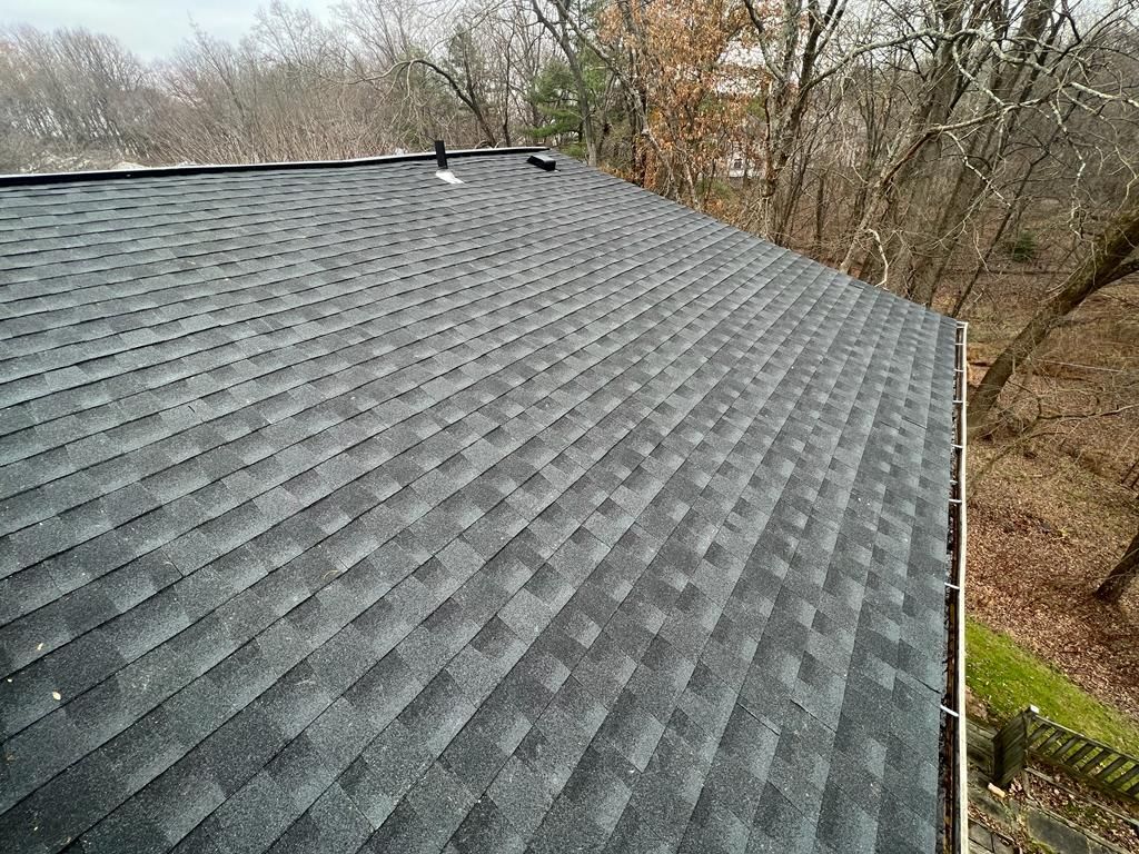 Gray shingled roof viewed from above, with trees and a yard in the background