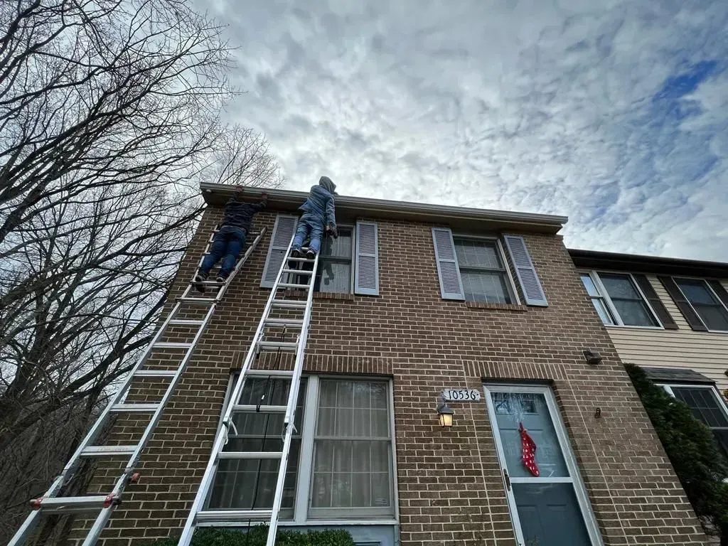 Worker on a ladder at the front of a brick townhouse under a cloudy sky