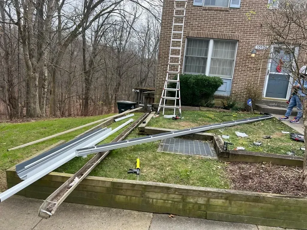 Metal beams and ladders laid across a lawn beside a brick house during a construction project