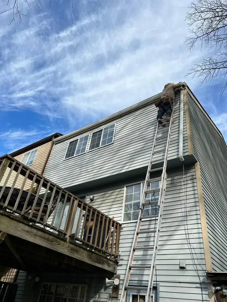 Two-story house with a ladder on the side and a wooden deck under a blue sky