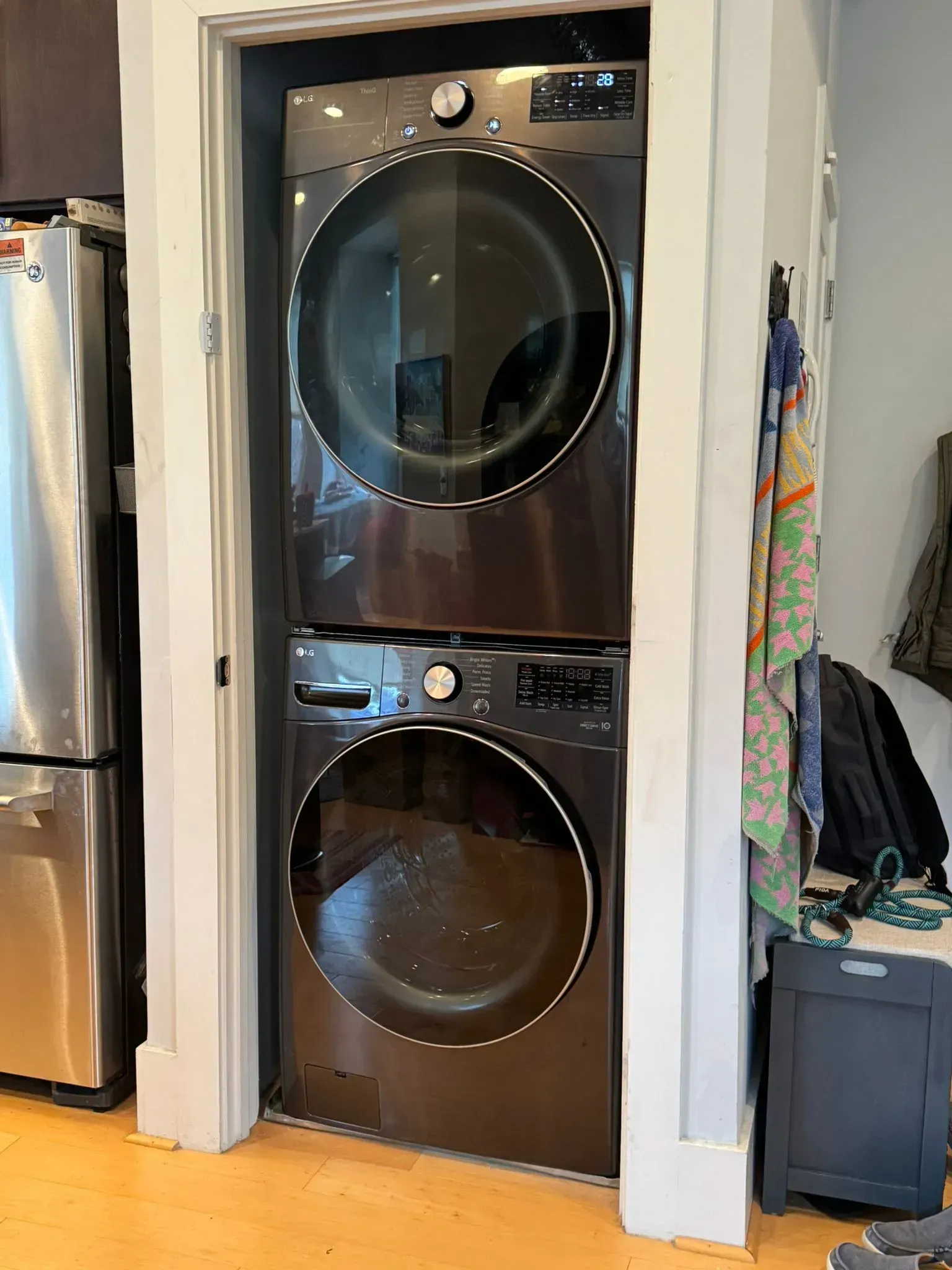 Stacked black washer and dryer in a narrow laundry closet with white trim